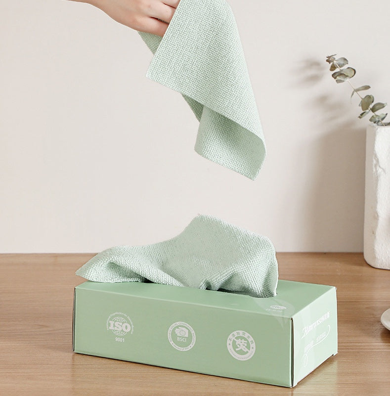 Green cleaning cloth being used to wipe a box on a wooden surface.