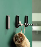 Black wall hook with a sponge hanging on it against a green wall.
