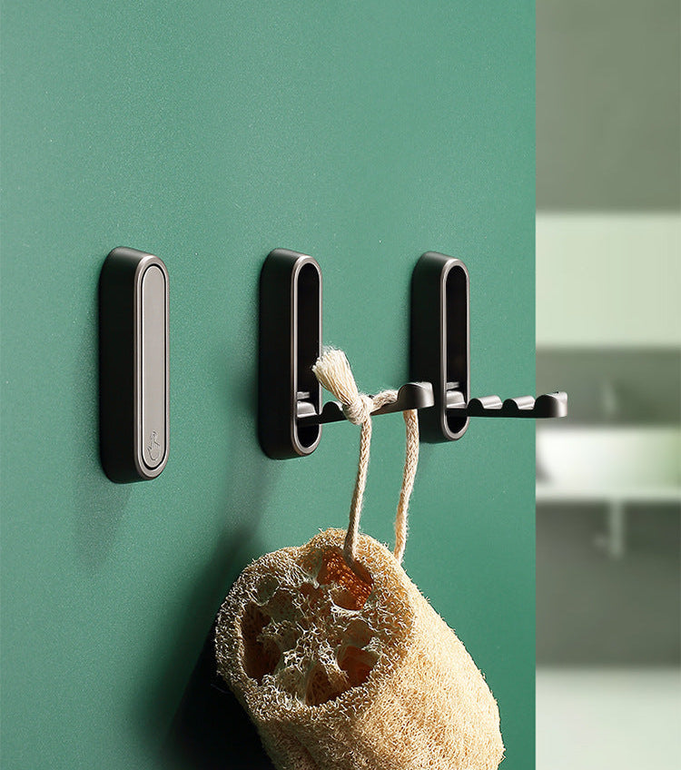 Black wall hook with a sponge hanging on it against a green wall.